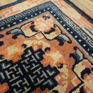Textured rug detail showing navy, rust, and cream patterns over distressed wood flooring.