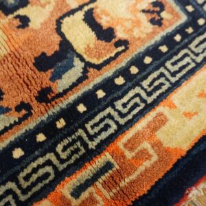 A high-pile rug with burnt orange and navy geometric patterns lies over worn wooden floorboards.