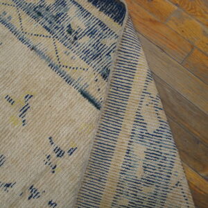 Cream flatweave rug with abstract blue and yellow patterns, folded over on distressed hardwood flooring.