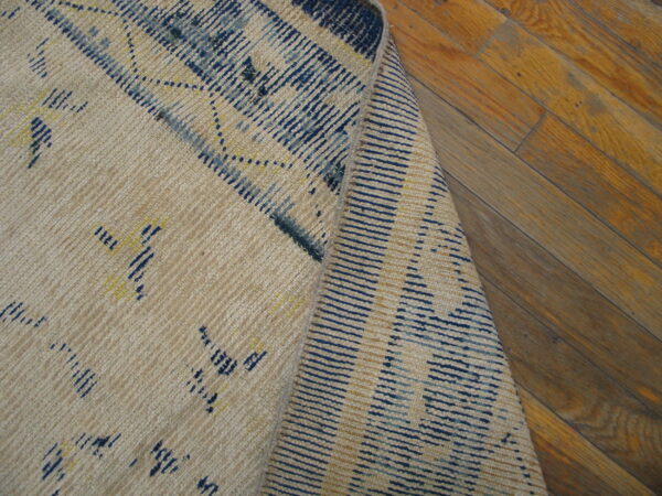Cream flatweave rug with abstract blue and yellow patterns, folded over on distressed hardwood flooring.
