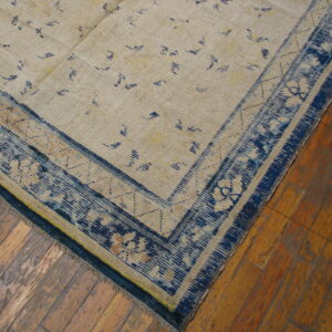 Low-pile beige rug with blue abstract field patterns and a wide ornamental blue border on wood flooring.