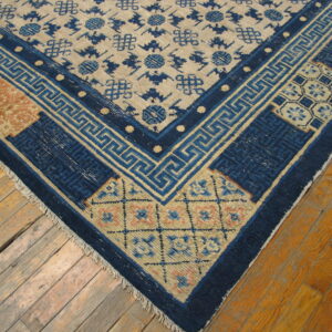 Tan rug with scattered blue motifs and a detailed blue and rust corner border rests on worn amber floorboards.