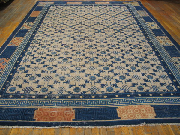 Beige field rug with dense indigo patterns and a wide multi-panel border over wood planks.