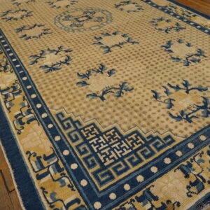 Tan rug with scattered blue foliage and prominent dark blue geometric borders on distressed wood floor.