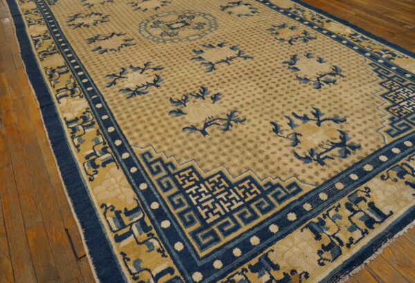 Tan rug with scattered blue foliage and prominent dark blue geometric borders on distressed wood floor.