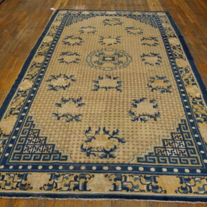 Light beige rug with deep blue borders and scattered geometric floral patterns rests on warm plank wood flooring.