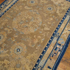 Tan and blue traditional rug displaying complex patterns and a geometric border on wood flooring.