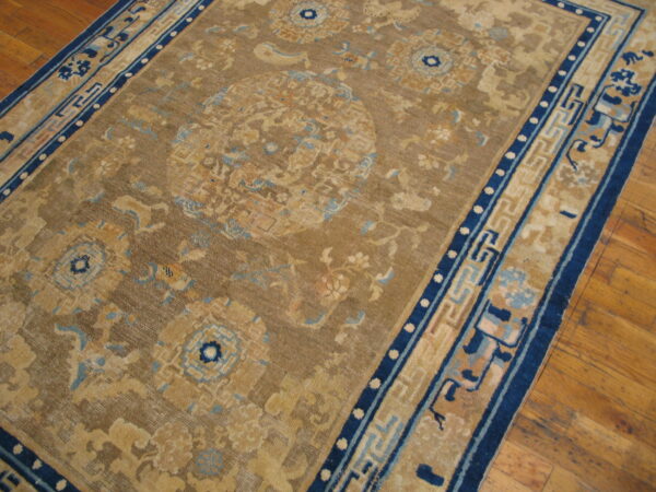Tan and blue traditional rug displaying complex patterns and a geometric border on wood flooring.