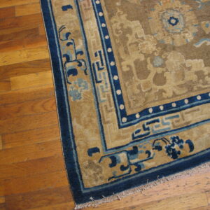 Tan rug with dark blue geometric borders and light blue accents resting on a wood floor.