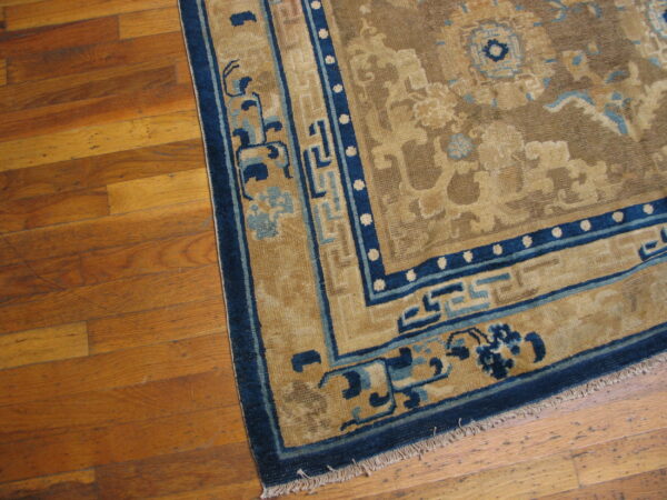 Tan rug with dark blue geometric borders and light blue accents resting on a wood floor.
