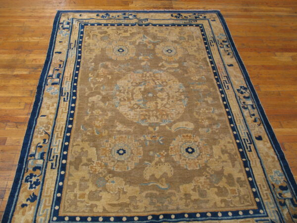Brown and tan rug featuring stylized blue and beige medallion and wide geometric borders rests on a hardwood floor.