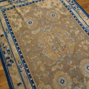 Low-pile rug in tan, brown, and indigo with traditional motifs rests on a light brown hardwood floor.