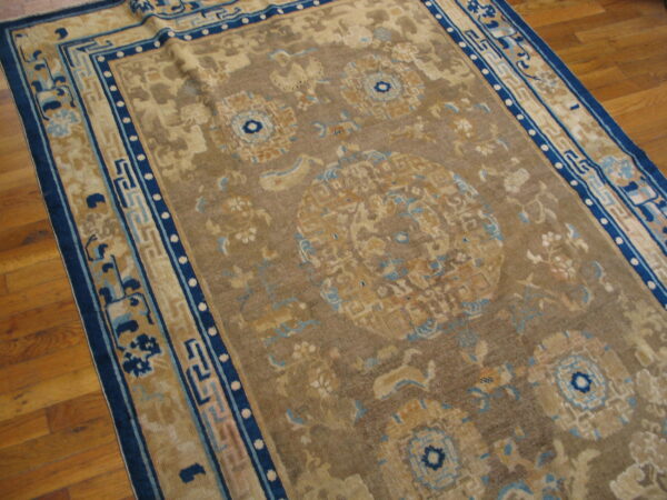 Low-pile rug in tan, brown, and indigo with traditional motifs rests on a light brown hardwood floor.