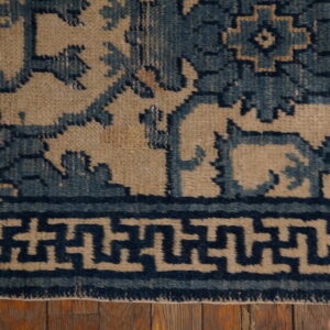 Blue geometric and floral patterned rug detail with a key border visible on rustic wood planks.