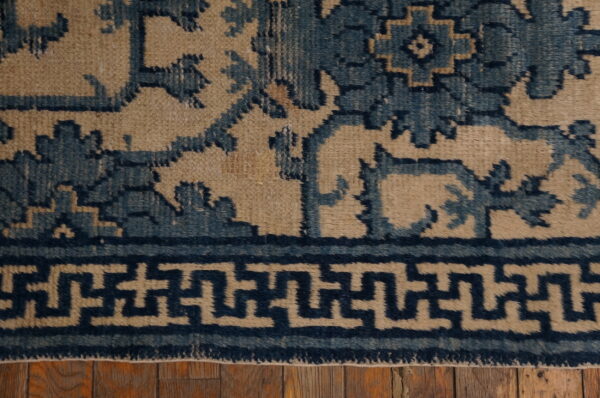 Blue geometric and floral patterned rug detail with a key border visible on rustic wood planks.