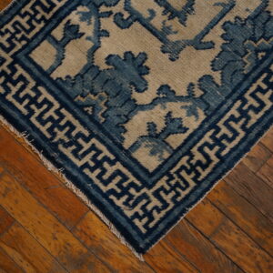 Blue and beige low-pile rug with geometric and floral patterns placed diagonally on distressed wood flooring.
