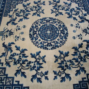 Cream rug with indigo floral motifs and geometric fretwork borders surrounding a central medallion.