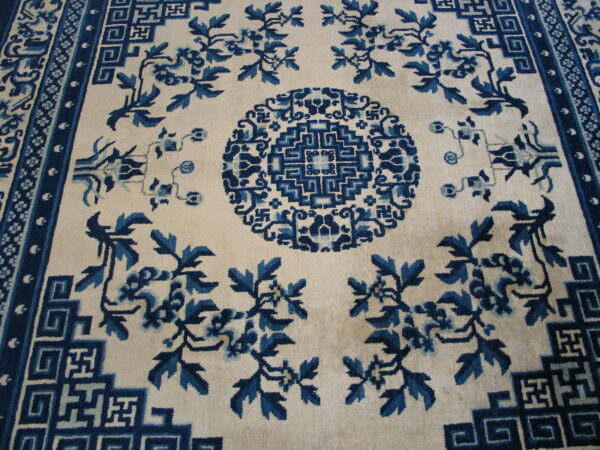 Cream rug with indigo floral motifs and geometric fretwork borders surrounding a central medallion.