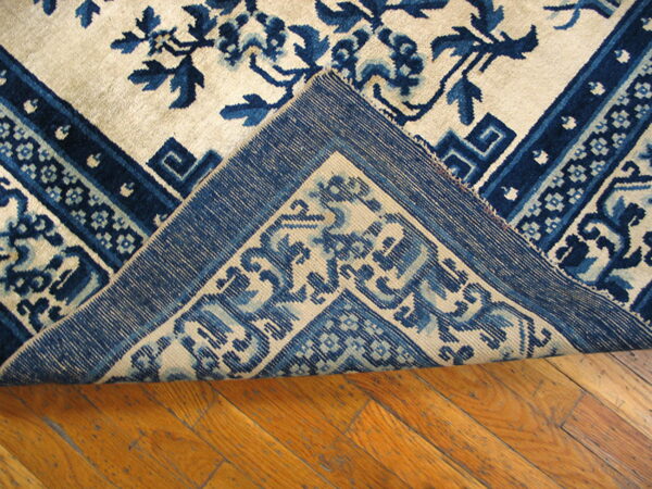 Cream rug with indigo blue floral and geometric patterns is folded over on distressed hardwood.