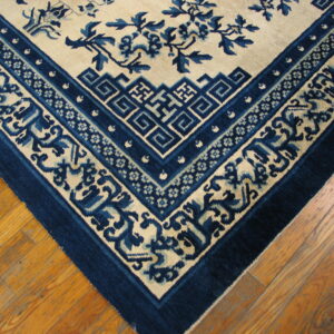 The corner of a low-pile cream rug with deep blue borders and a floral pattern on wooden flooring.