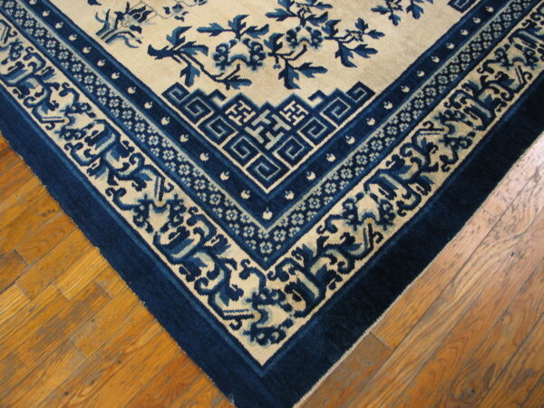 The corner of a low-pile cream rug with deep blue borders and a floral pattern on wooden flooring.