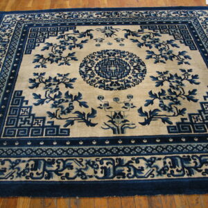 A high-contrast blue and beige rug featuring floral motifs and geometric borders on a light brown wood floor.