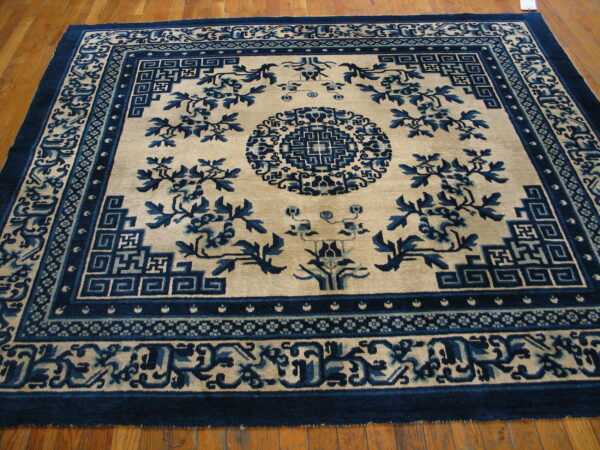 A high-contrast blue and beige rug featuring floral motifs and geometric borders on a light brown wood floor.