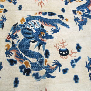 Close-up of a pale ivory rug featuring a stylized blue dragon motif accented with rust and gold.