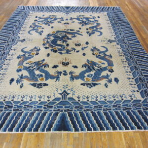 Cream rug with blue dragon pattern and elaborate wave border on glossy wood flooring.