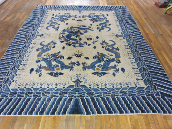 Cream rug with blue dragon pattern and elaborate wave border on glossy wood flooring.