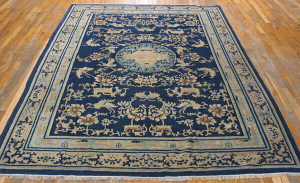 Navy blue rug with tan floral and animal motifs, plus a central medallion, rests on wood flooring.