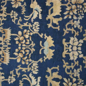 Detailed view of a navy blue rug featuring gold and light blue stylized floral and scrollwork motifs.
