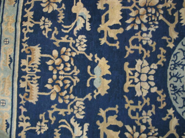 Detailed view of a navy blue rug featuring gold and light blue stylized floral and scrollwork motifs.