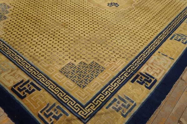 Yellow rug featuring navy blue fretwork borders and a repeating dotted field pattern lies on wooden plank flooring.