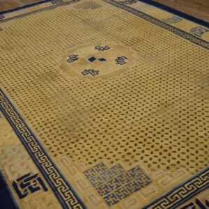 A yellow rug with a dark spotted field and navy geometric borders rests on wood floorboards.