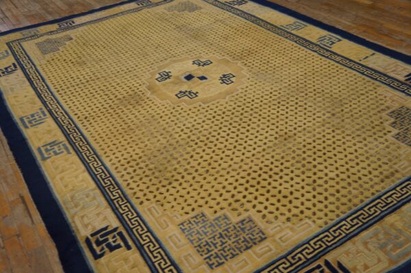 A yellow rug with a dark spotted field and navy geometric borders rests on wood floorboards.