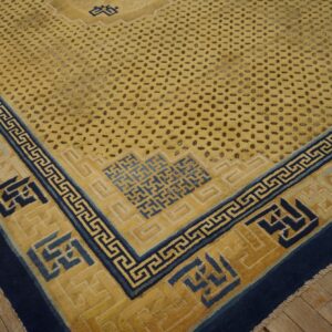 Saffron rug with a dotted field, navy Greek key borders, and geometric fretwork, laid on wood planks.