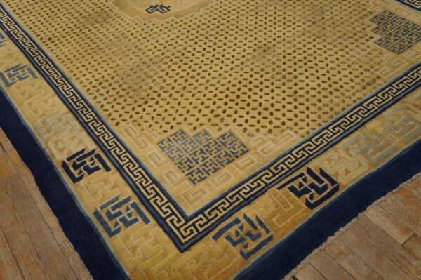 Saffron rug with a dotted field, navy greek key borders, and geometric fretwork, laid on wood planks.