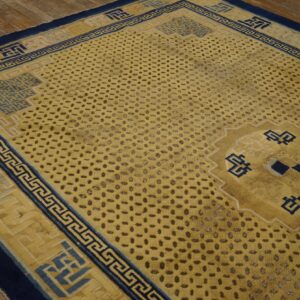 Golden yellow rug with navy blue geometric borders and a speckled field pattern on rustic wood flooring.