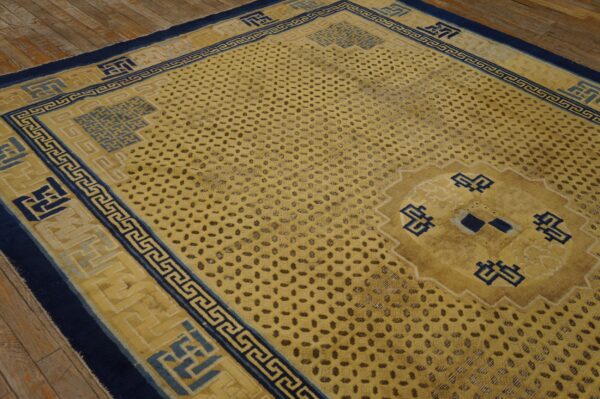Golden yellow rug with navy blue geometric borders and a speckled field pattern on rustic wood flooring.
