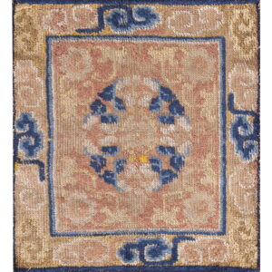 Muted tan, pink, and navy blue rug fragment displaying a central circular motif and patterned borders.