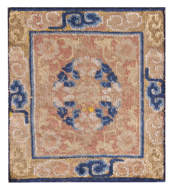 Muted tan, pink, and navy blue rug fragment displaying a central circular motif and patterned borders.