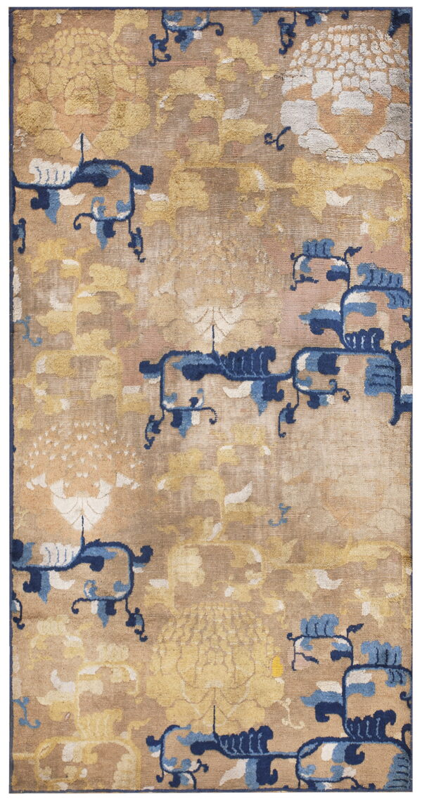 Tan rug with large, faded golden floral patterns and scattered dark and light blue stylized motifs.