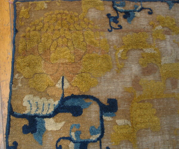 Textured rug detail shows yellow and blue floral motifs on a tan ground beside wood flooring.