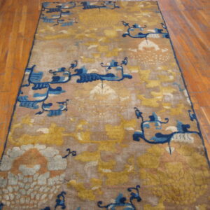Golden yellow and tan runner rug with stylized blue abstract patterns rests on wooden plank flooring.