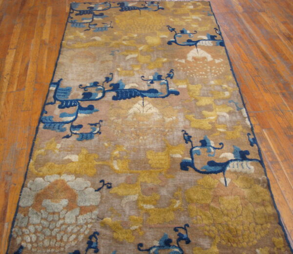 Golden yellow and tan runner rug with stylized blue abstract patterns rests on wooden plank flooring.