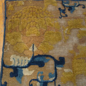 Detailed view of a textured rug with golden yellow and navy floral motifs beside worn wood planks.