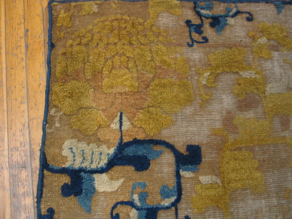 Detailed view of a textured rug with golden yellow and navy floral motifs beside worn wood planks.