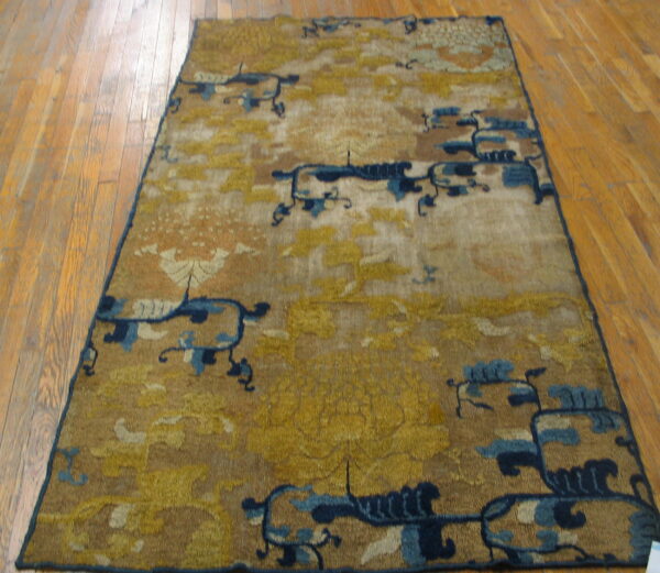 Low-pile, rectangular rug featuring gold, tan, and dark blue abstract designs on hardwood flooring.