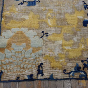 Distressed yellow, light blue, and tan rug corner featuring stylized motifs on gray wood floor.